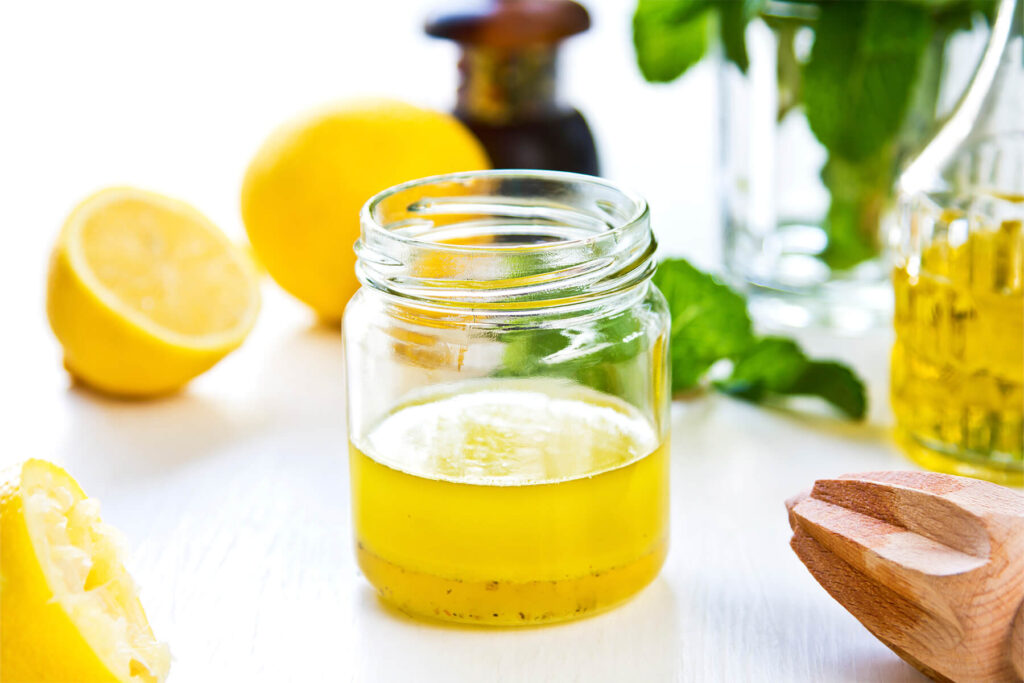 Helle Honig-Zitronen-Vinaigrette mit frischer Minze in einem kleinen Glas, daneben halbierte Zitronen und ein Holzpresser