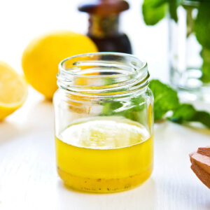 Helle Honig-Zitronen-Vinaigrette mit frischer Minze in einem kleinen Glas, daneben halbierte Zitronen und ein Holzpresser