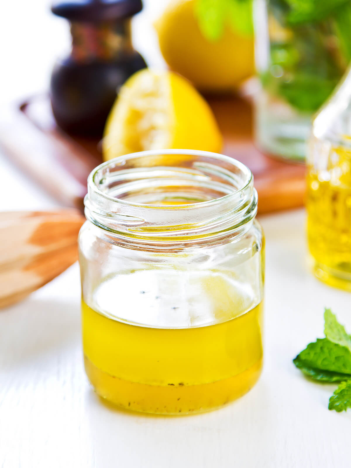 Kleines Glas mit heller Honig-Zitronen-Vinaigrette, deutlich in eine goldene Saft- und eine hellere Ölschicht getrennt, daneben Zitronen und Minze