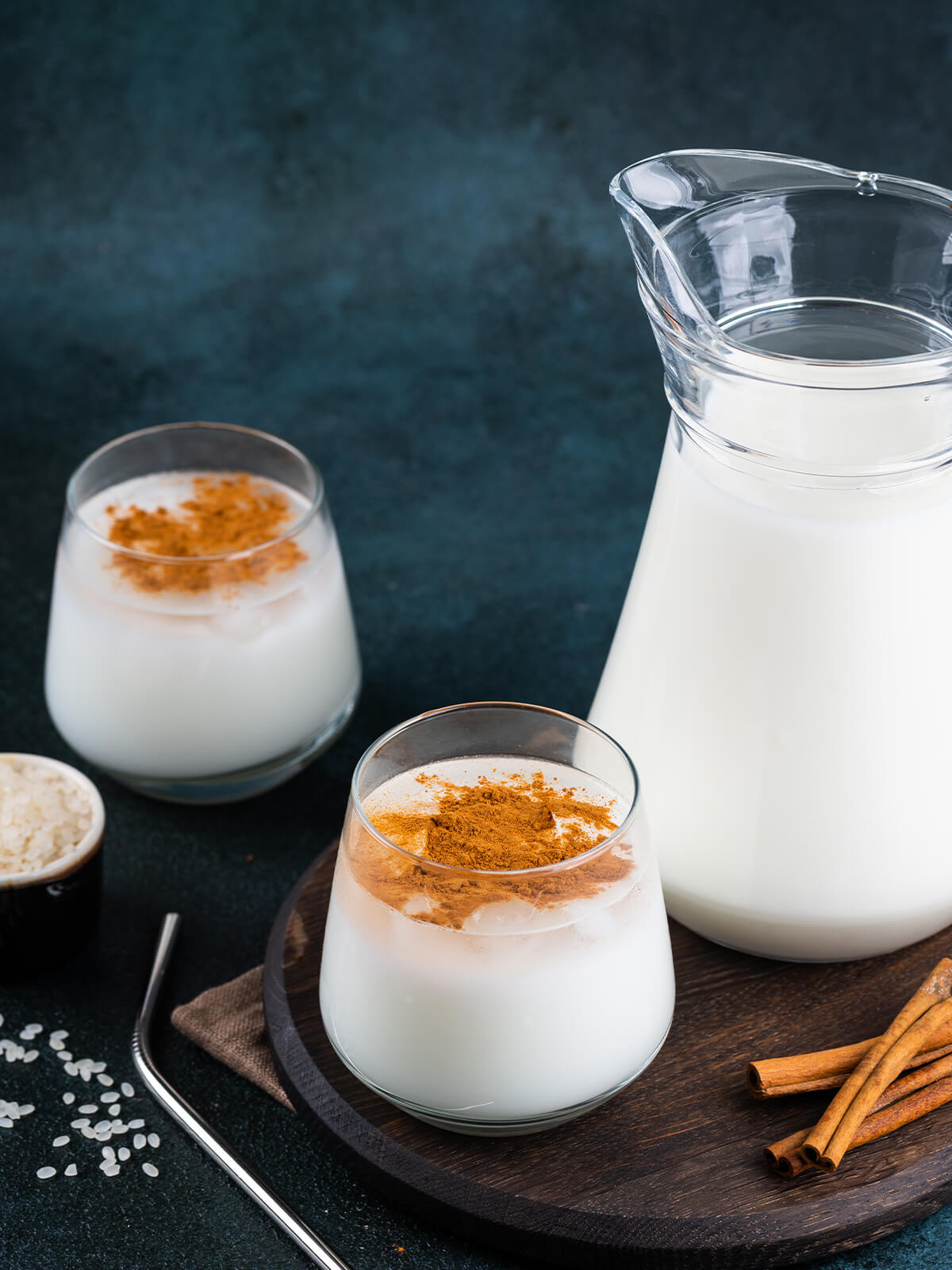 Zwei Gläser mexikanische Horchata mit Zimt und eine Glaskanne, dazu Zimtstangen und Reis