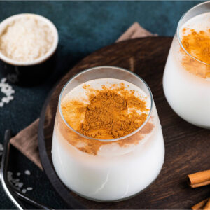 Zwei Gläser Horchata de Arroz mit gemahlenem Zimt obenauf, daneben Reis und Zimtstangen
