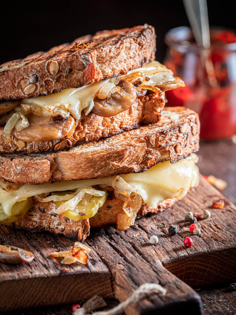 Geröstetes Käse-Sandwich mit geschmolzenem Käse, Champignons, Zwiebeln und Gewürzgurken im Anschnitt gestapelt