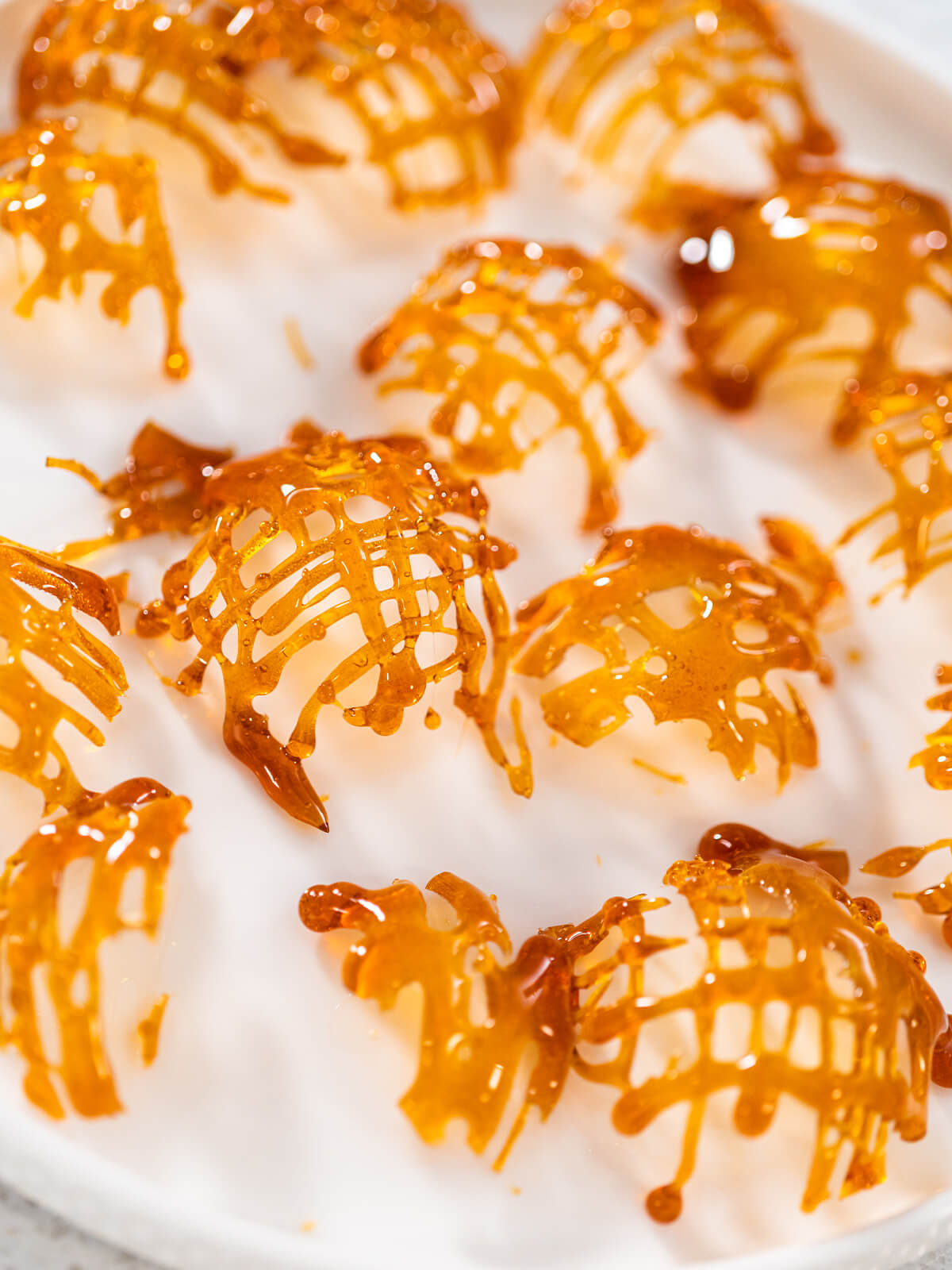 Mehrere fertige, goldbraune Karamellgitter als Cupcake-Topper auf einem weißen Teller angerichtet