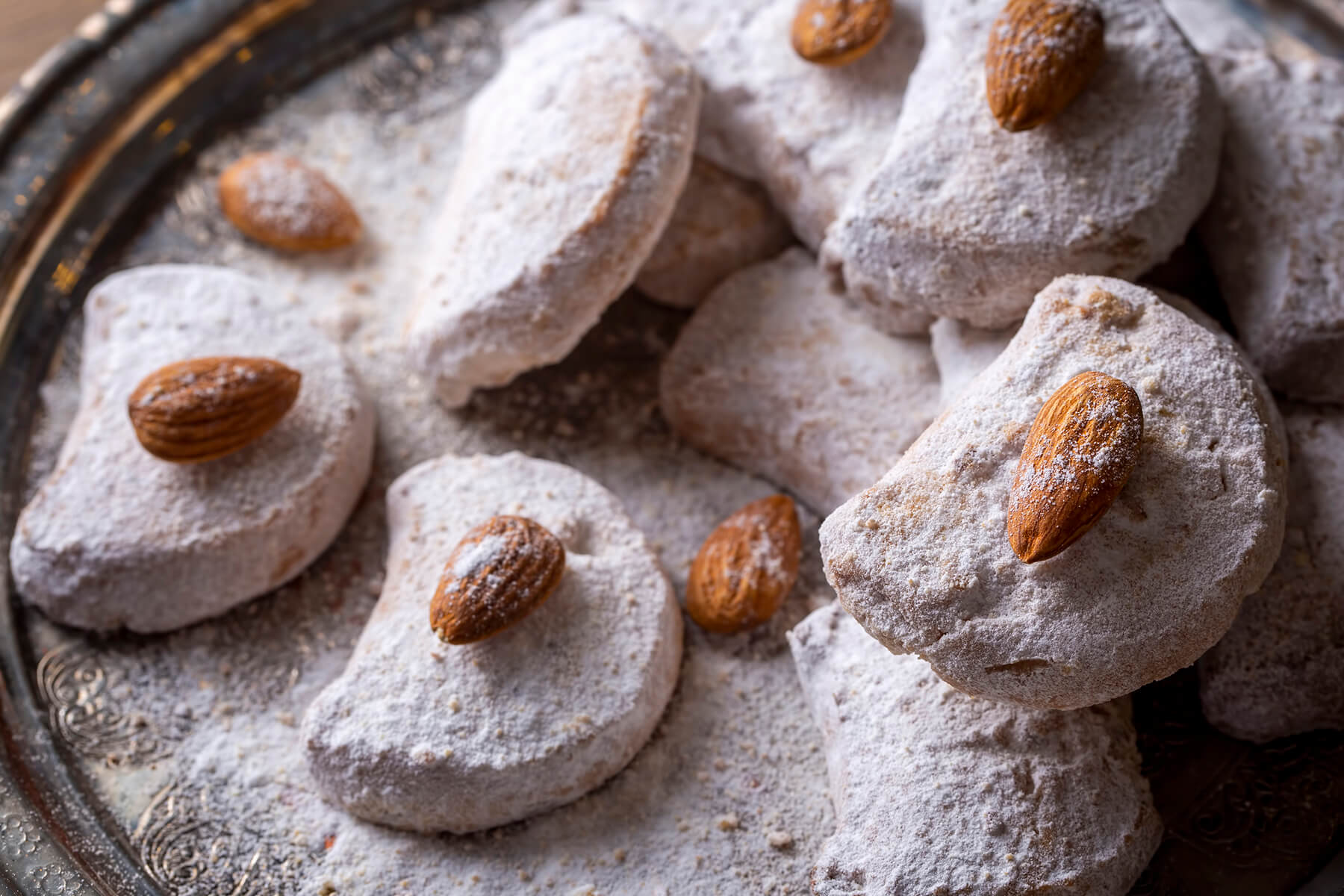 Geformte Kavala Cookies in Halbmondform auf einer silbernen Platte, jeder mit einer eingedrückten ganzen Mandel