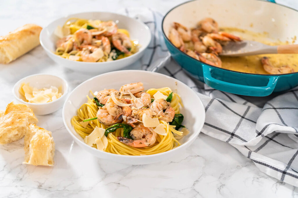 Fertige Garnelen-Spaghetti mit Spinat und Parmesan in Schalen, dahinter die Pfanne