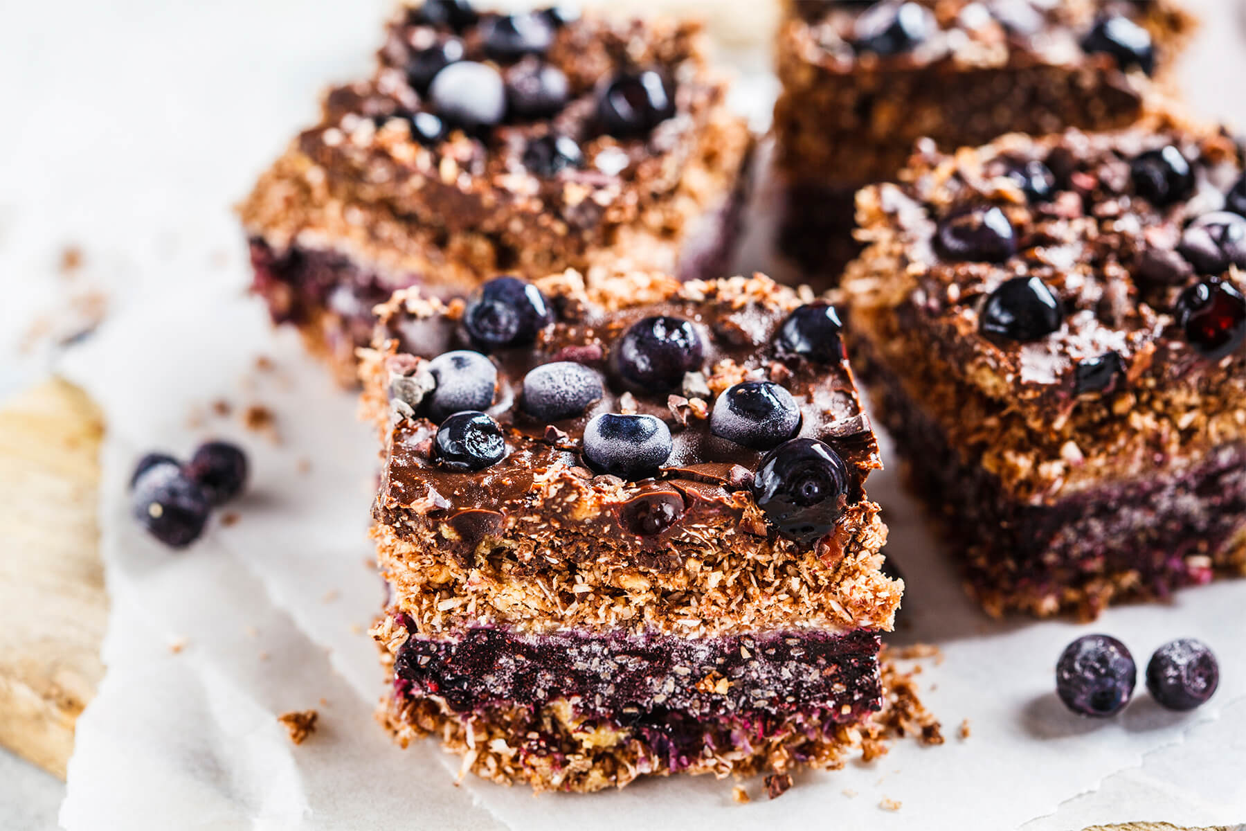 Vegane Kokos-Schoko-Schnitten mit Blaubeeren, seitlich fotografiert mit vier sichtbaren Lagen im Anschnitt