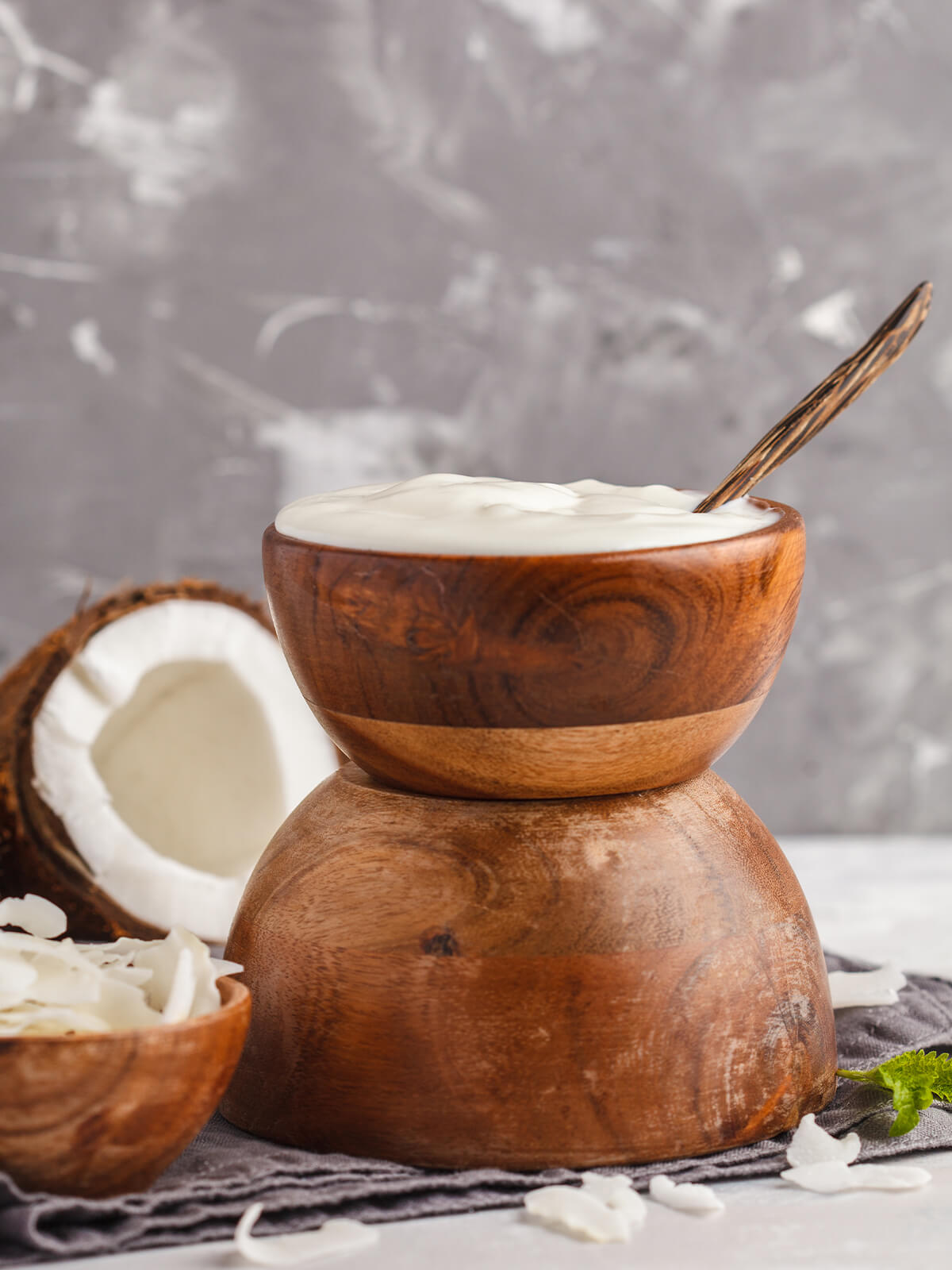 Cremiger veganer Kokosjoghurt in einer gestapelten Holzschale mit Löffel, daneben eine kleine Schale mit Kokoschips