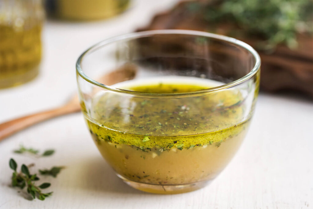 Cremige Kräuter-Senf-Vinaigrette in einer Glasschale mit vielen fein gehackten frischen Kräutern, daneben ein Löffel