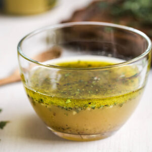 Cremige Kräuter-Senf-Vinaigrette in einer Glasschale mit vielen fein gehackten frischen Kräutern, daneben ein Löffel
