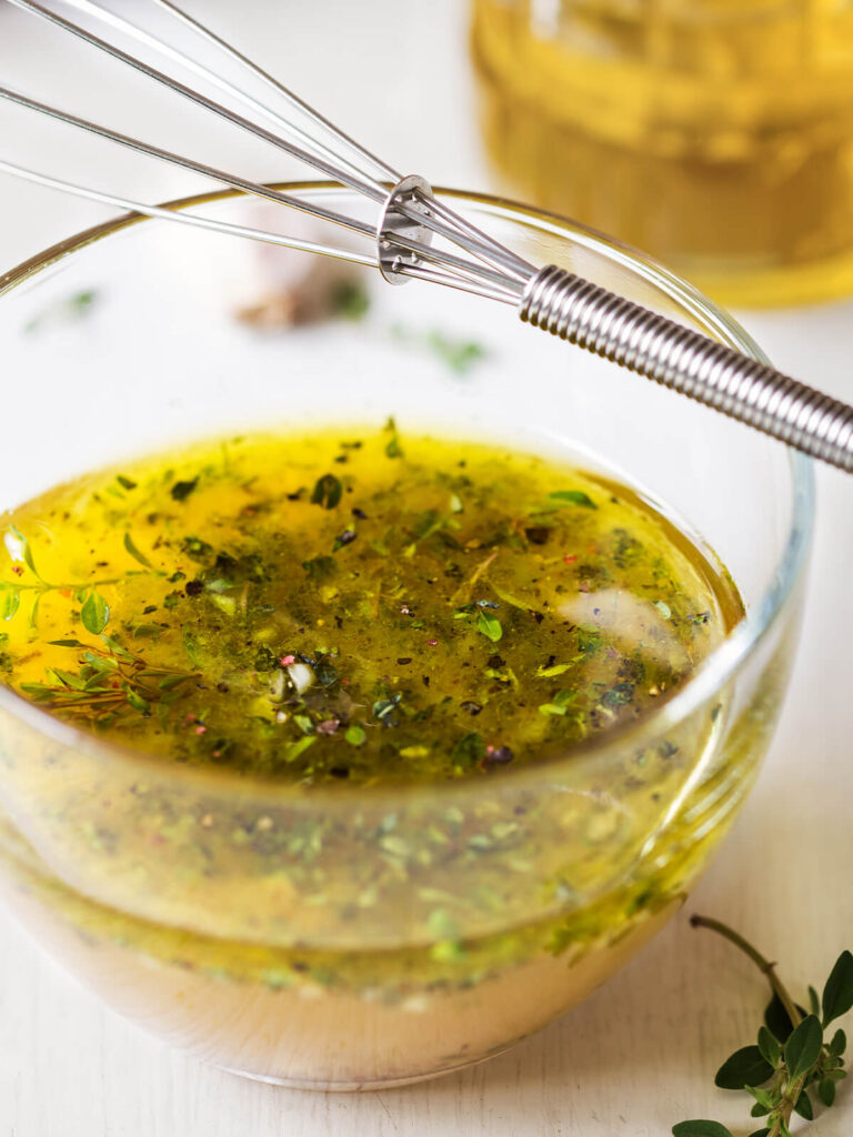 Kräuter-Senf-Vinaigrette wird in einer Glasschale mit einem Schneebesen aufgeschlagen, mit frischen Kräutern und Thymian