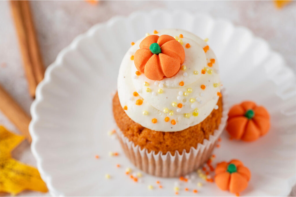 Fertiger Kürbis-Cupcake von oben mit glatten Frosting-Ringen, Fondant-Kürbis und bunten Zuckerperlen