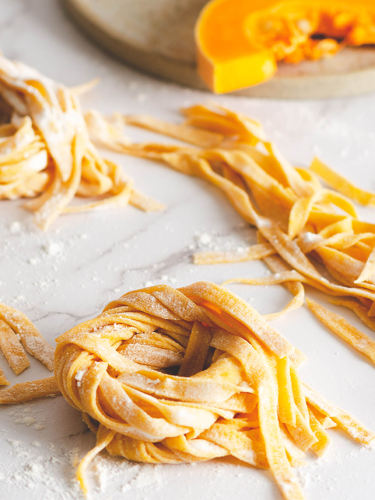Frische Kürbis-Bandnudeln aus Butternut zu einem Nest gedreht, daneben ein Stück Butternut-Kürbis