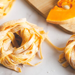Frische Kürbis-Bandnudeln aus Butternut zu Nestern gedreht, daneben ein Stück Butternut-Kürbis