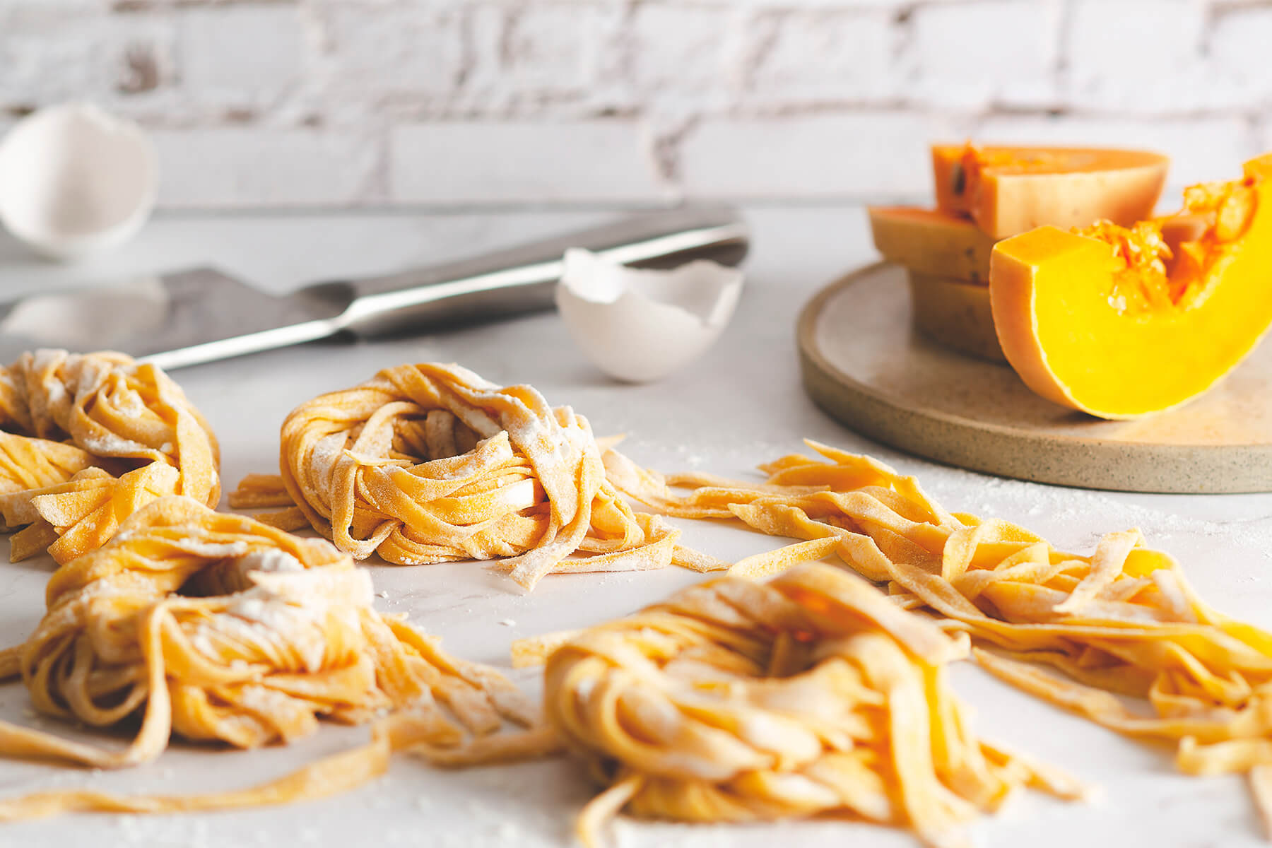 Frische Kürbis-Nudelnester auf Marmor, daneben Eierschalen und ein Stück Butternut-Kürbis