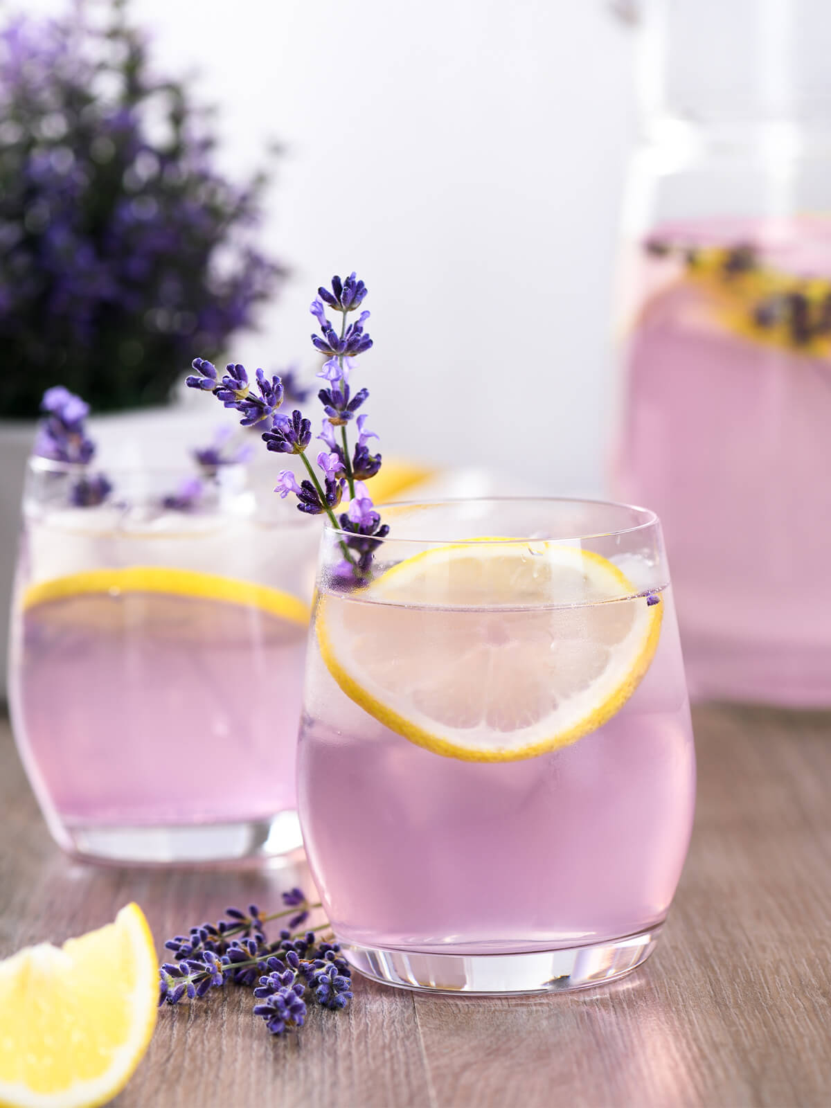 Zwei Gläser lila Lavendellimonade mit Zitronenscheiben und frischen Lavendelrispen auf einem Holztisch