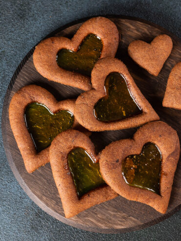 Herzförmige Lebkuchen-Plätzchen mit bernsteinfarbenem Bonbon-Fenster auf einem runden Holzbrett