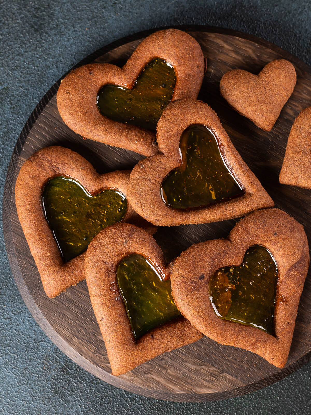 Herzförmige Lebkuchen-Plätzchen mit bernsteinfarbenem Bonbon-Fenster auf einem runden Holzbrett