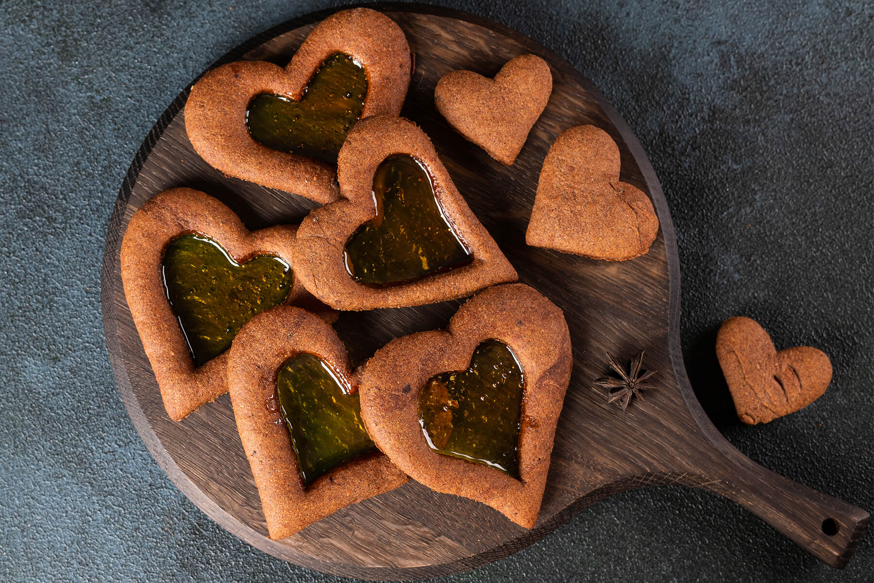 Mehrere Lebkuchen-Herzen mit bernsteinfarbenem Fenster und kleine schlichte Herzen auf einem Holzbrett