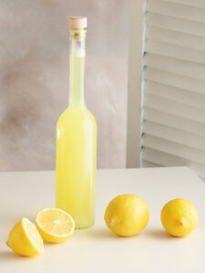 Flasche mit selbst gemachter Zitronen-Ingwer-Limonade neben frischen Zitronen auf hellem Untergrund
