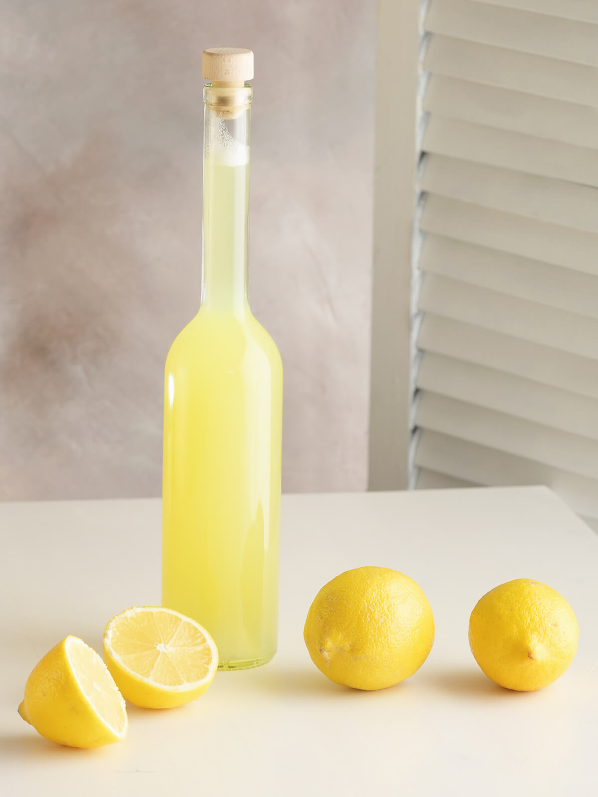 Flasche mit selbst gemachter Zitronen-Ingwer-Limonade neben frischen Zitronen auf hellem Untergrund