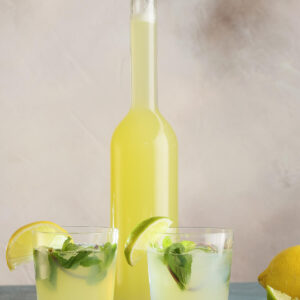 Zwei Gläser selbst gemachte Zitronen-Ingwer-Limonade mit Minze und Eis vor einer Flasche mit Sirup