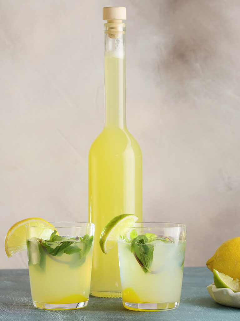 Zwei Gläser selbst gemachte Zitronen-Ingwer-Limonade mit Minze und Eis vor einer Flasche mit Sirup