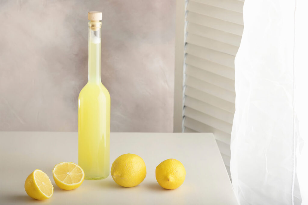 Flasche mit selbst gemachter Zitronenlimonade neben aufgeschnittenen und ganzen Zitronen auf hellem Tisch