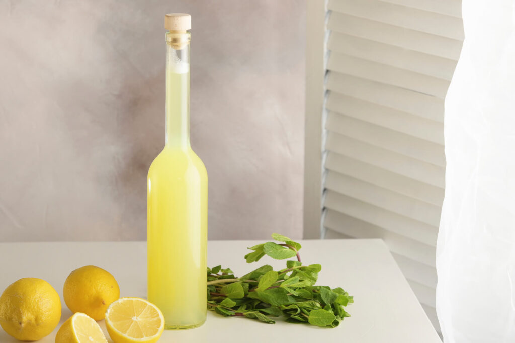 Flasche mit Zitronen-Ingwer-Limonade neben frischen Zitronen und einem Bund Minze auf hellem Tisch