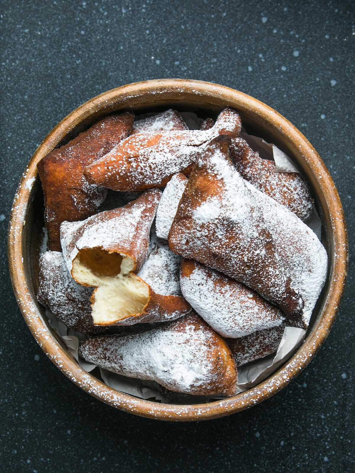 Aufgebrochenes Mandazi mit luftig-weicher Krume in einer Schale mit weiteren Stücken und Puderzucker