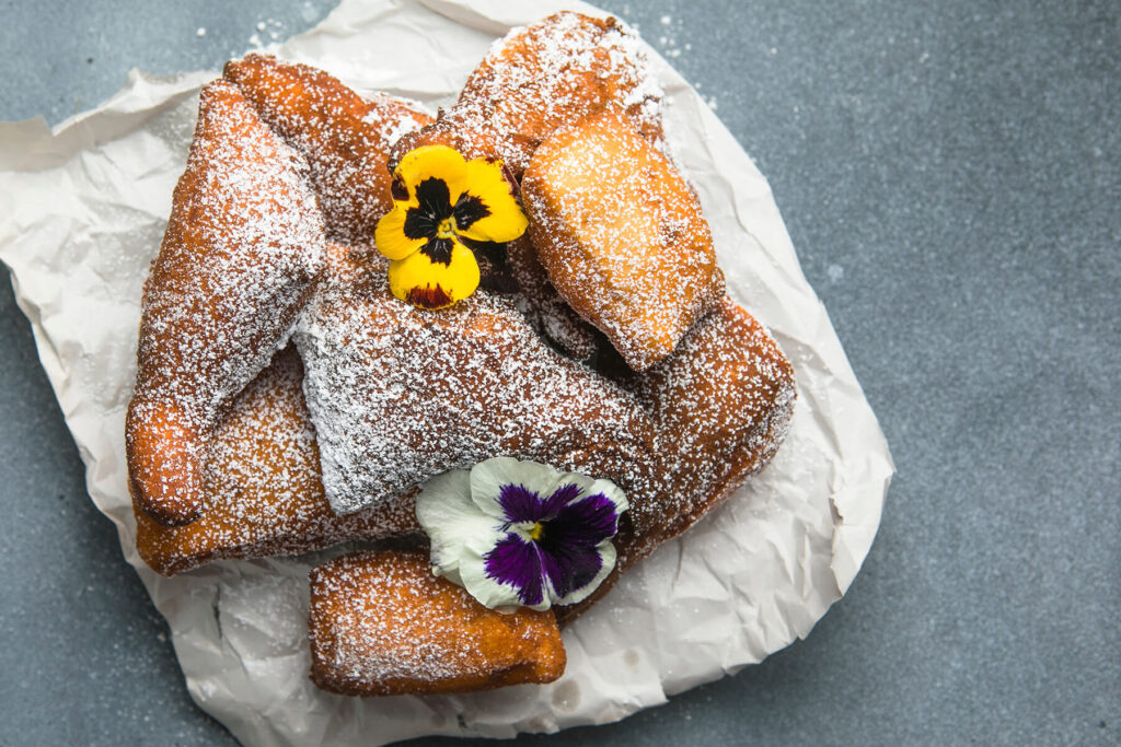 Fertige Mandazi mit Puderzucker bestäubt und essbaren Blüten von oben angerichtet