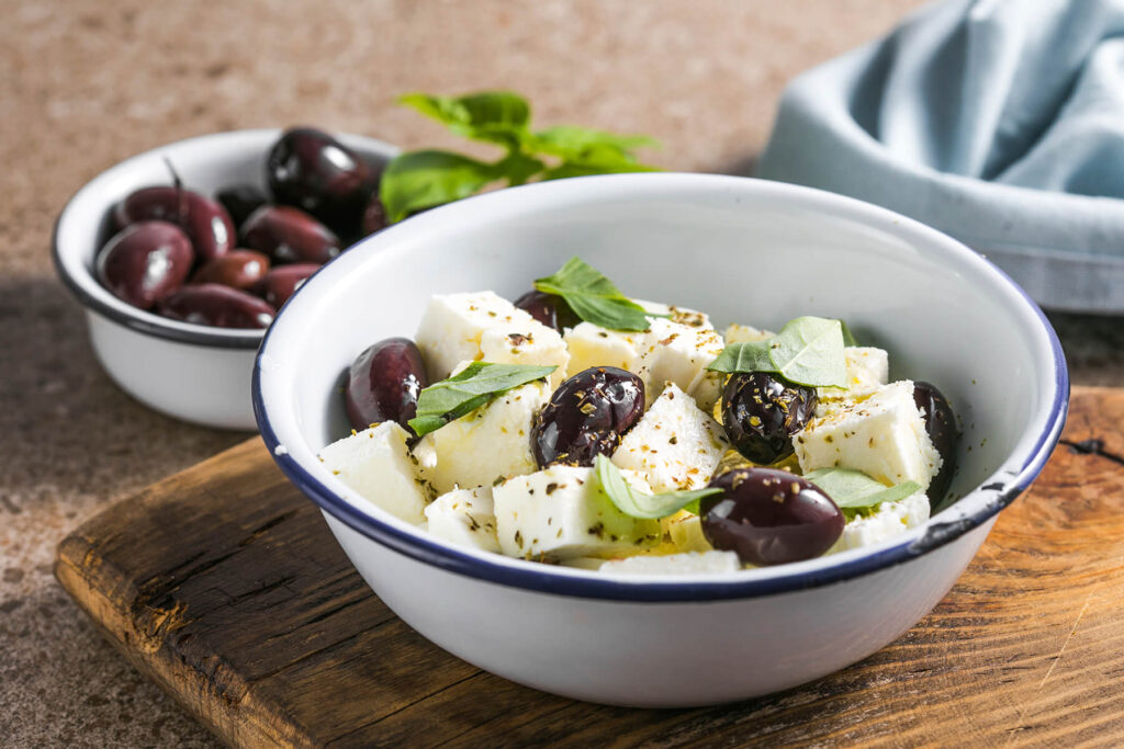 Marinierter Feta in Würfeln mit Kalamata-Oliven, Basilikum und Oregano in einer Emailleschale
