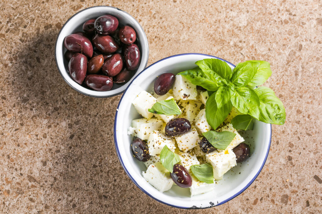 Fertig marinierter Feta mit Kalamata-Oliven, Oregano und Basilikum von oben in einer Schale