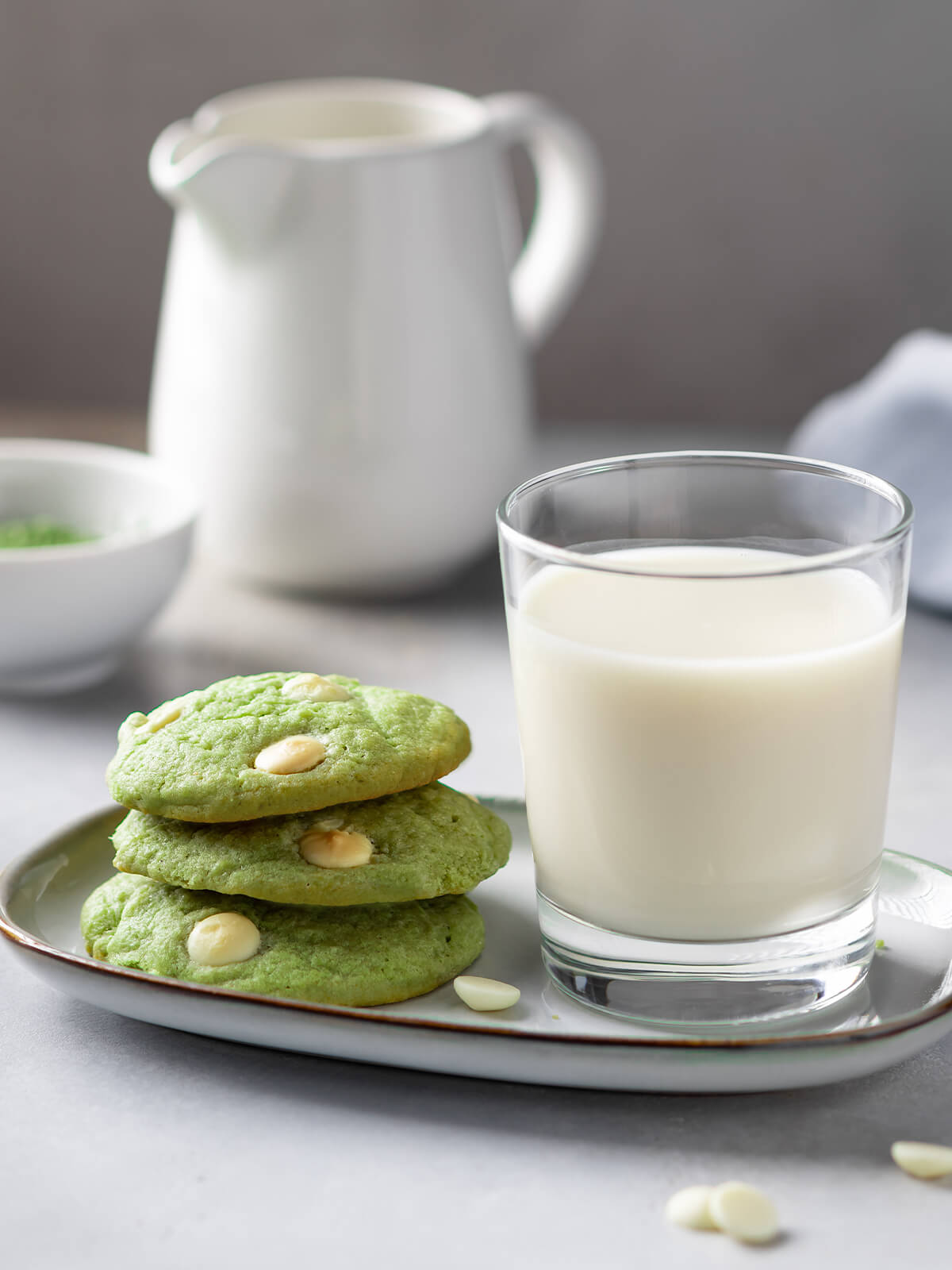 Gestapelte grüne Matcha-Cookies mit weißer Schokolade neben einem Glas Milch auf einem Teller