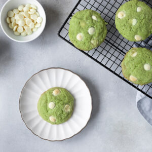 Grüne Matcha-Cookies mit weißer Schokolade auf einem Kühlgitter und einem Teller, daneben Matcha-Pulver