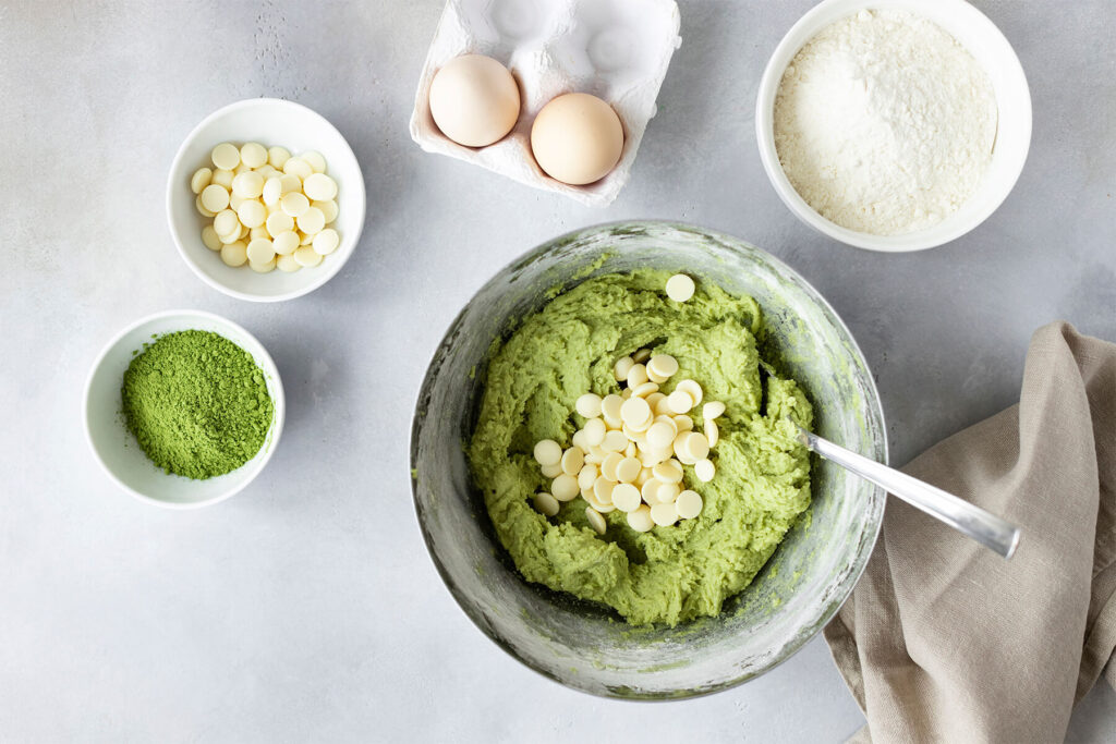 Weiße Schokotropfen werden unter den grünen Matcha-Keksteig in der Schüssel gehoben