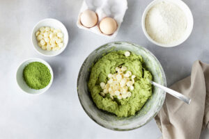 Weiße Schokotropfen werden unter den grünen Matcha-Keksteig in der Schüssel gehoben
