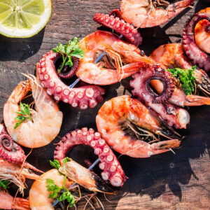 Gegrillte Meeresfrüchte-Spieße mit Garnelen und Oktopus, Petersilie und Zitrone auf einem Holzbrett