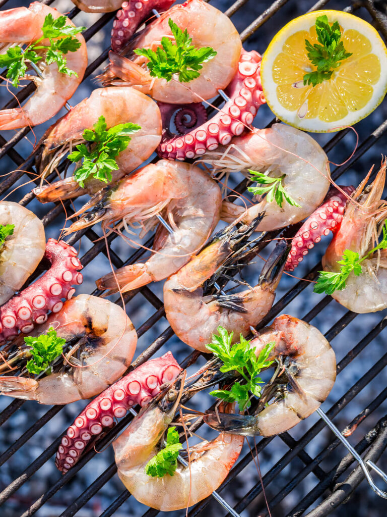 Rohe Garnelen und Oktopus-Tentakel mit Petersilie auf dem Holzkohlegrill