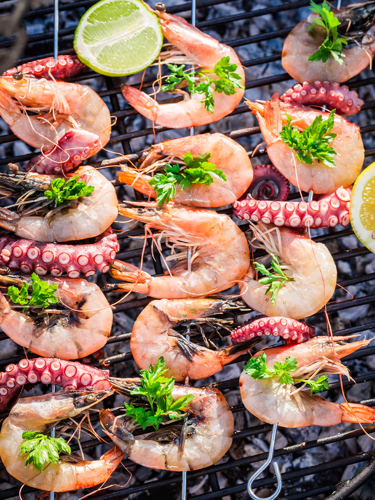 Garnelen- und Oktopus-Spieße mit Zitrone und Petersilie beim Grillen über Holzkohle