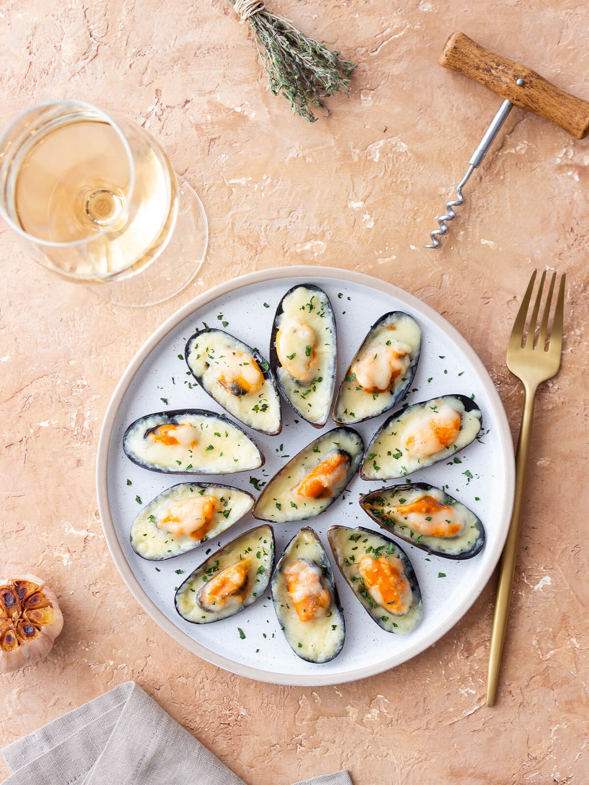 Überbackene Miesmuscheln in der halben Schale mit Käse und Petersilie, dazu Weißwein, Thymian und geröstete Knoblauchknolle