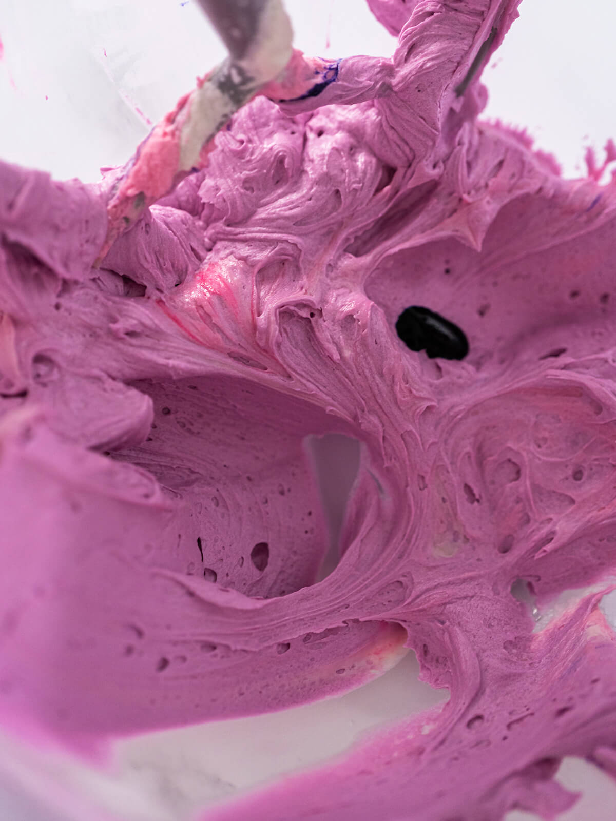 Buttercreme wird zu einem Beere-Ton gemischt, ein Tropfen Farbe wird gerade untergerührt