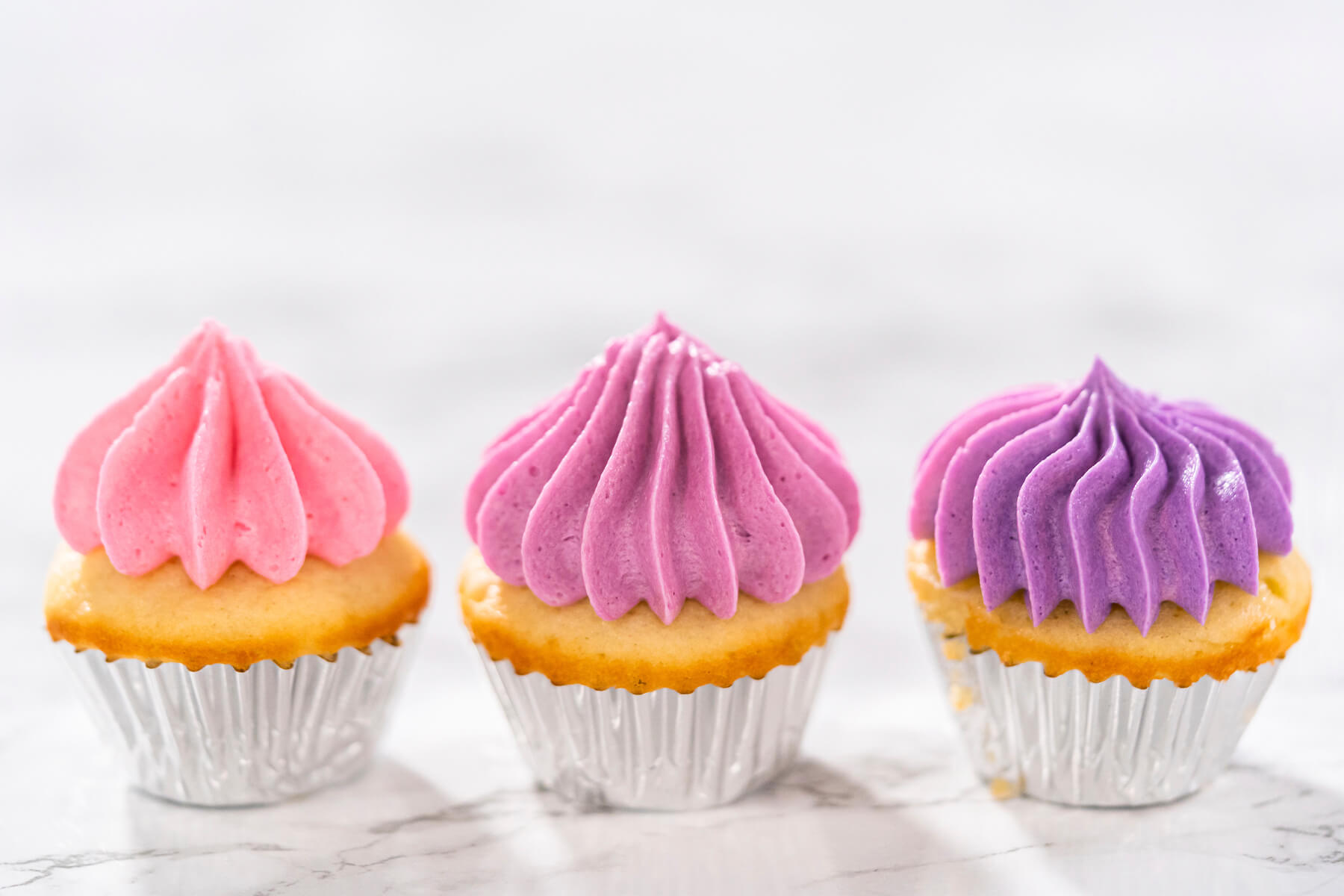 Drei Mini-Cupcakes nebeneinander mit Buttercreme in Rosa, Beere und Violett zeigen den Ombre-Verlauf