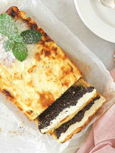 Angeschnittener Mohn-Quark-Kuchen als Kastenkuchen mit goldener Kruste, daneben zwei Scheiben mit dünnem Mürbeteigboden, dicker dunkler Mohnschicht und heller Quarkmasse darüber, bestäubt mit Puderzucker und mit Minze garniert