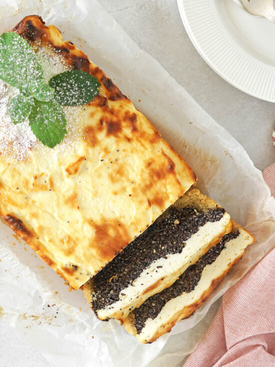 Angeschnittener Mohn-Quark-Kuchen als Kastenkuchen mit goldener Kruste, daneben zwei Scheiben mit dünnem Mürbeteigboden, dicker dunkler Mohnschicht und heller Quarkmasse darüber, bestäubt mit Puderzucker und mit Minze garniert