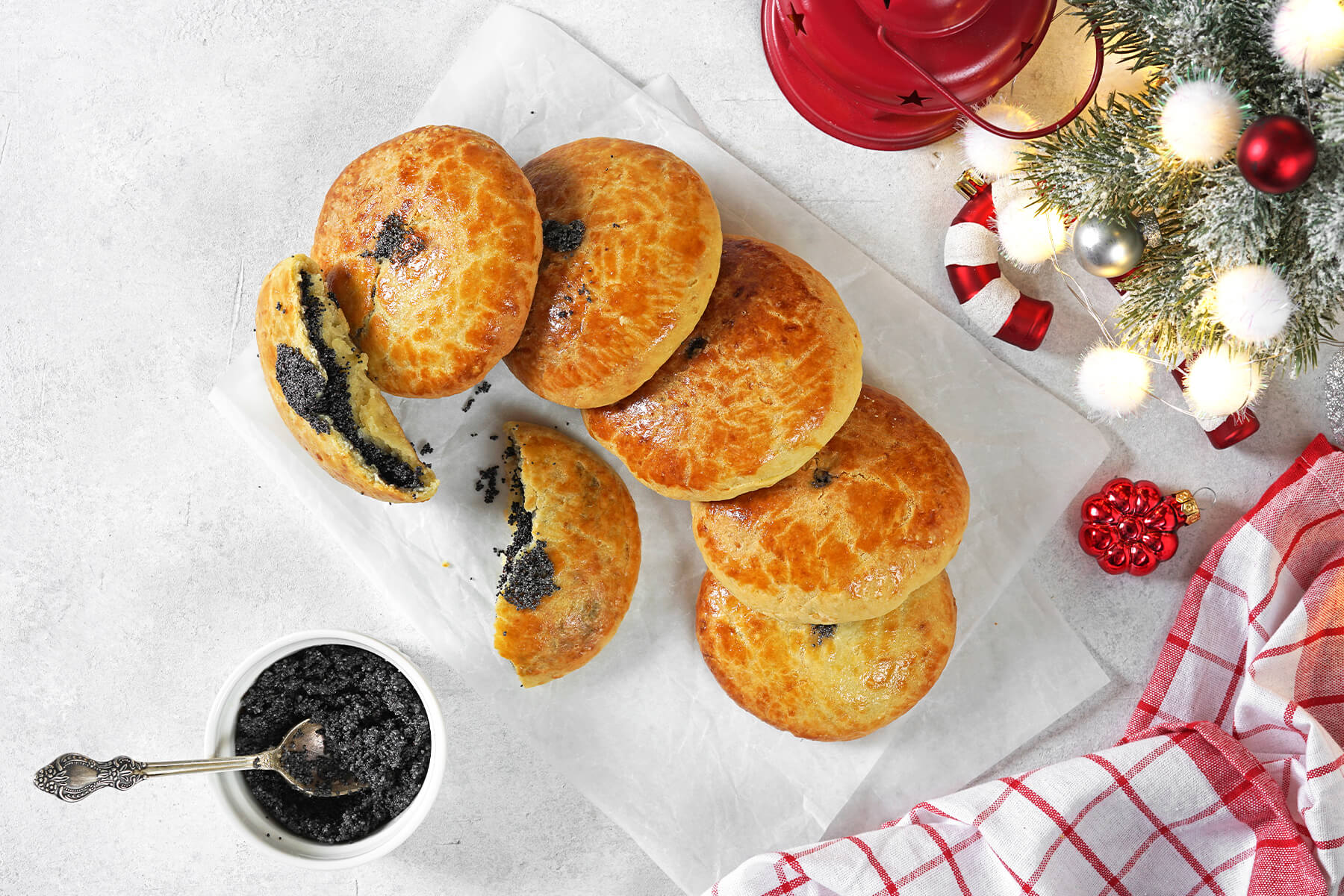 Draufsicht auf mehrere Mohnzelten mit aufgebrochenen Stücken, daneben ein Schälchen gemahlener Mohn mit Löffel und Weihnachtsdeko