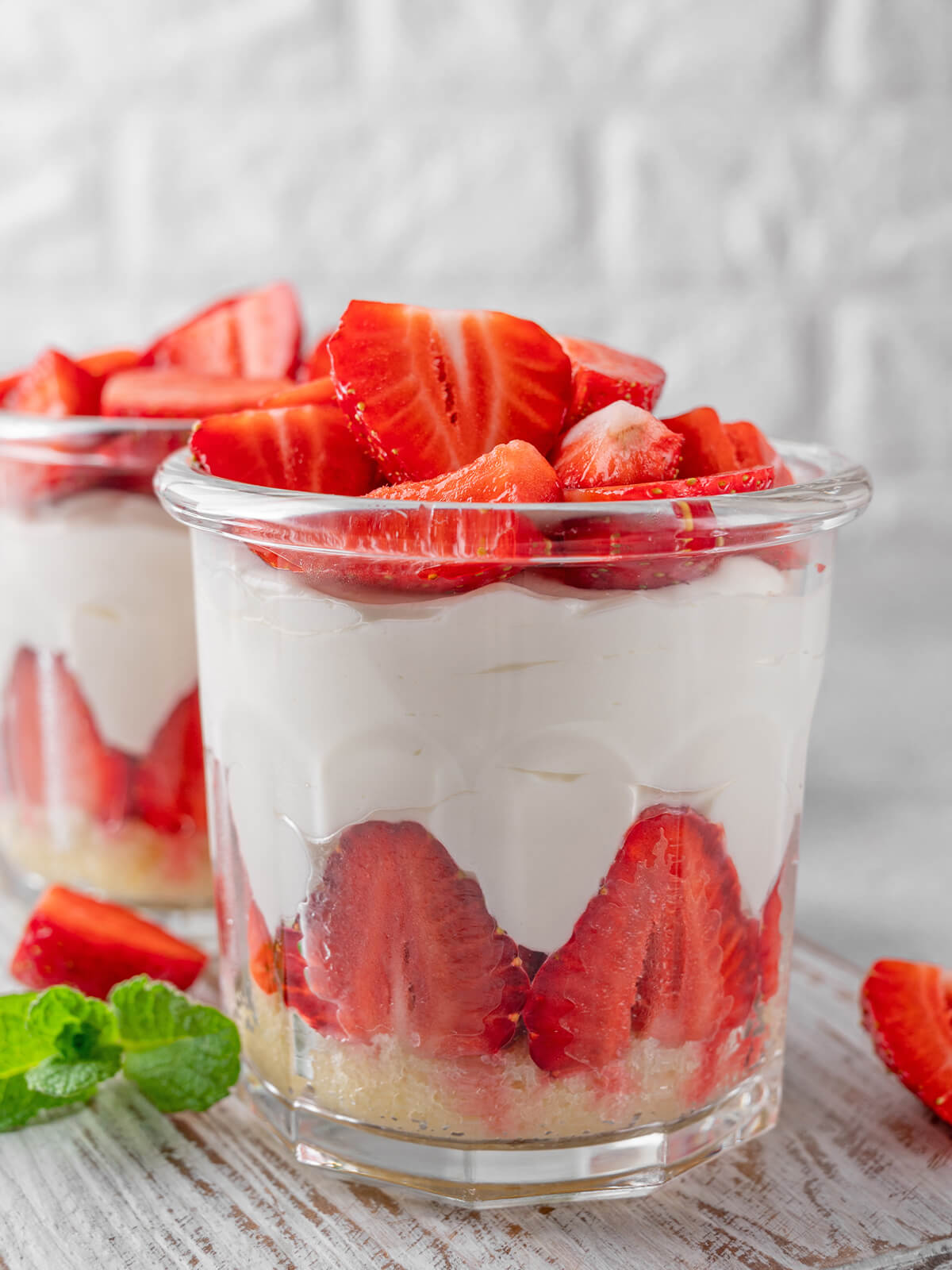 No-Bake Erdbeer-Cheesecake in großen Gläsern von vorn mit hellem Butterkeks-Boden, einem deutlich sichtbaren Kranz aus halbierten Erdbeeren an der Glaswand, luftiger Frischkäsecreme und einem Berg frischer Erdbeeren obenauf