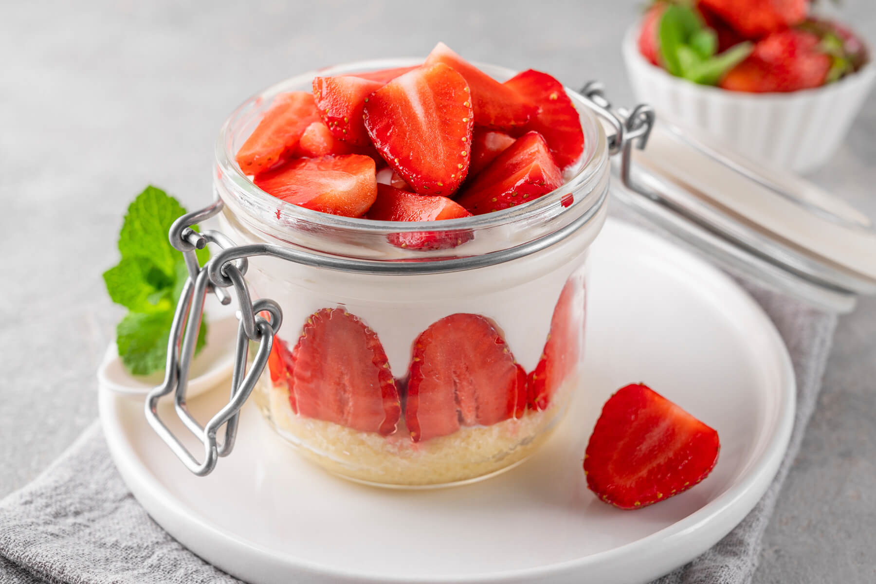 No-Bake Erdbeer-Cheesecake im Bügelglas mit hellem Keksboden und einem gleichmäßigen Kranz aus halbierten Erdbeeren, die mit der Schnittfläche und dem Stielende nach oben an der Glaswand sitzen