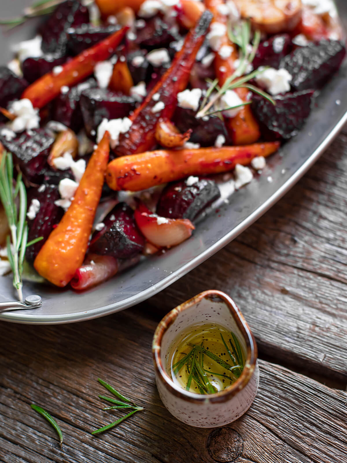 Nahaufnahme von ofengerösteter Rote Bete mit Möhren und Feta, daneben ein Kännchen mit Rosmarin-Olivenöl