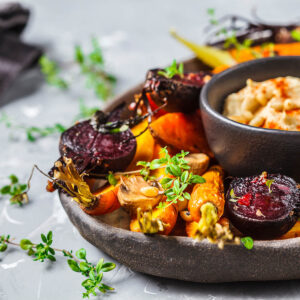 Buntes Ofengemüse mit roter Bete, Karotten und Champignons auf einem Teller, dazu eine Schale Hummus