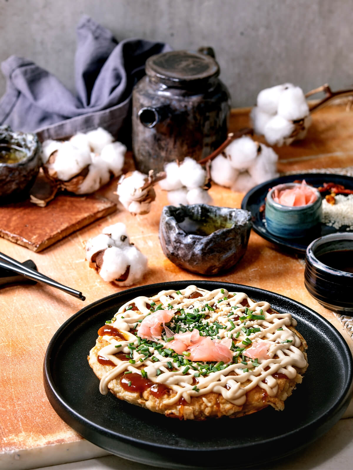 Japanischer Kohl-Pfannkuchen Okonomiyaki mit Mayonnaise-Gitter und rosa eingelegtem Ingwer, angerichtet auf dunklem Teller
